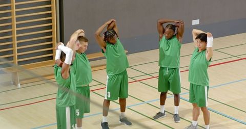 Diverse male basketball team warming up with overhead stretches on indoor court
