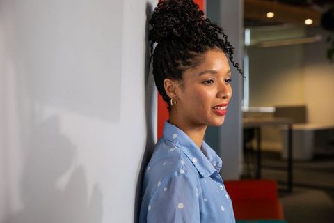 African american professional woman leaning against wall in coworking space, smiling