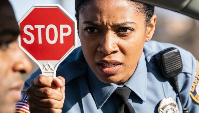Police officer holding stop paddle and showing badge during traffic stop closeup