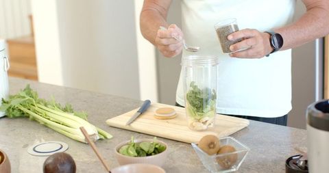 Preparing green smoothie with chia seeds, spinach, banana in personal blender cup