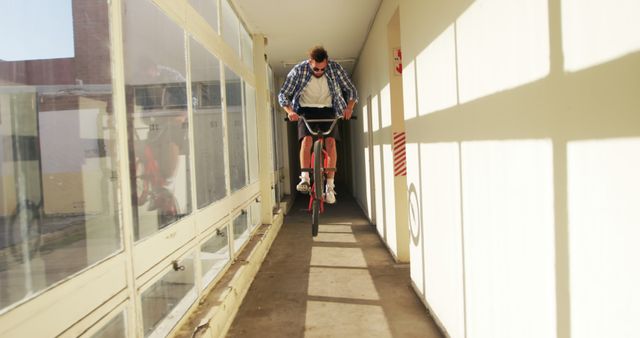 Young man performing an impressive bicycle stunt by jumping in an indoor corridor. His fearless and adventurous nature is highlighted. Could be used in contexts related to extreme sports, athleticism, adventure activities, or urban lifestyle brands.