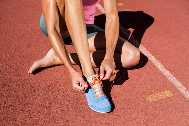 Female athlete tying her running shoes on running track