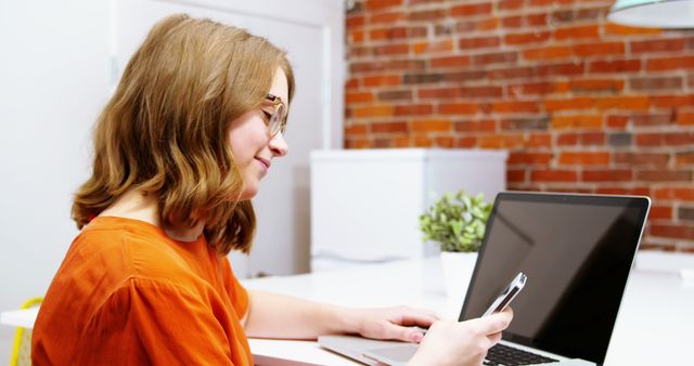 Young Woman Smiling While Using Smartphone and Laptop in Modern Office - Download Free Stock Images Pikwizard.com