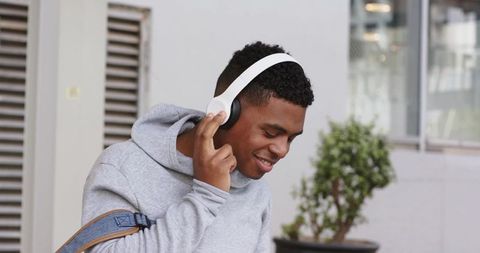 Young man enjoying music with white headphones and denim bag on urban street