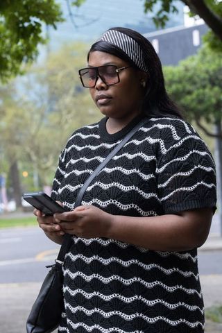 Woman standing on city sidewalk texting on smartphone wearing patterned knit top and headband