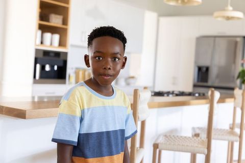 African american boy standing in bright modern kitchen wearing colorful striped t-shirt