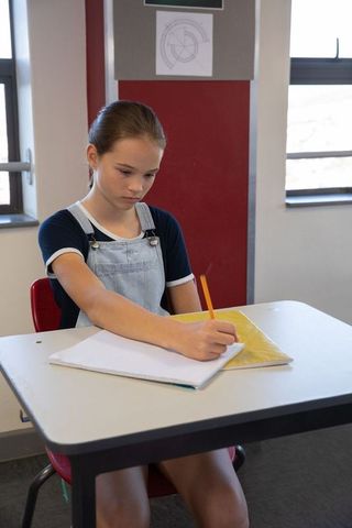 Teen student writing in classroom, focused acoustic learning environment