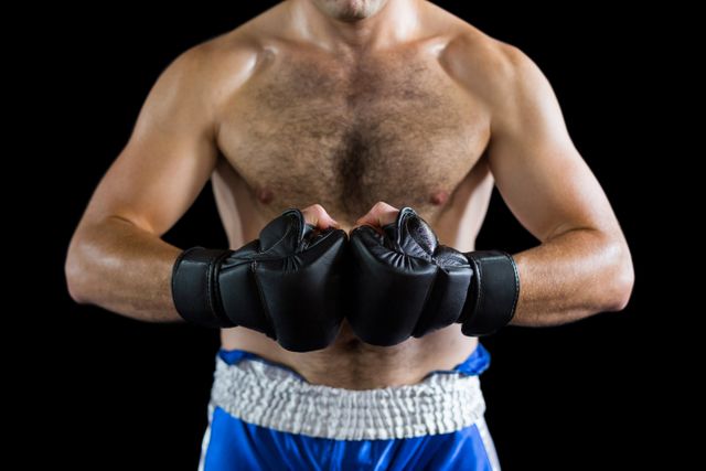 Mid section of a boxer wearing black gloves and blue shorts, performing a boxing stance against a black background. Ideal for use in sports and fitness promotions, training materials, motivational posters, and articles related to boxing and physical fitness.