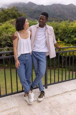 Multicultural couple leaning on balcony overlooking misty mountains wearing casual jeans
