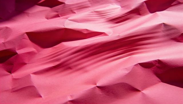 Crumpled magenta paper texture showing deep creases and soft light shadows closeup