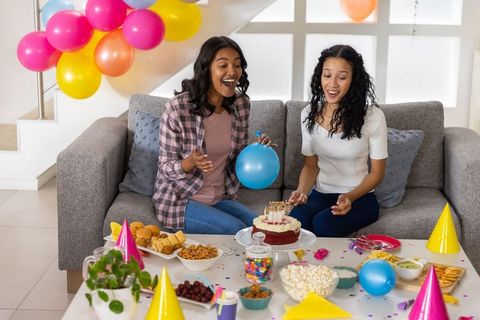Diverse mother and teenage daughter celebrating birthday with cake and colorful balloons