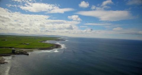 Overlooking coastal farmland and rocky headlands from drone with harbor pier and open sea