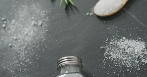 Salt shaker and granules on dark stone countertop