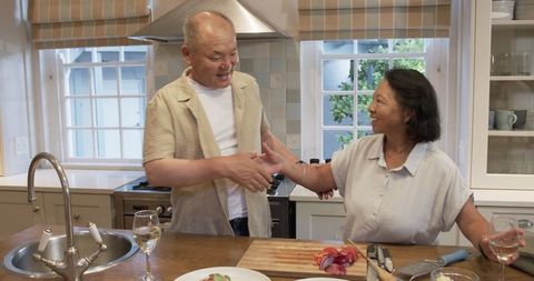 Senior Couple Celebrating in Kitchen, Smiling and Toasting Wine