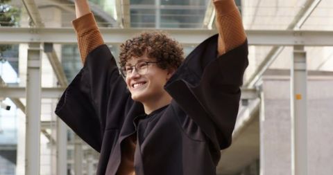 Graduate raising arms and smiling under glass canopy celebrating graduation achievement