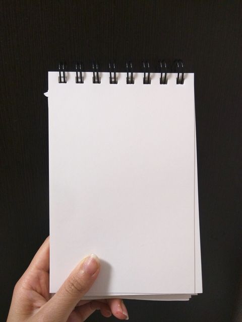 Image features a hand holding a spiral-bound blank notebook with a dark background. Useful for themes related to education, note-taking, writing, sketching, stationary products and creativity. Ideal for illustrating blank space concepts, organization tools, and classroom or study materials.