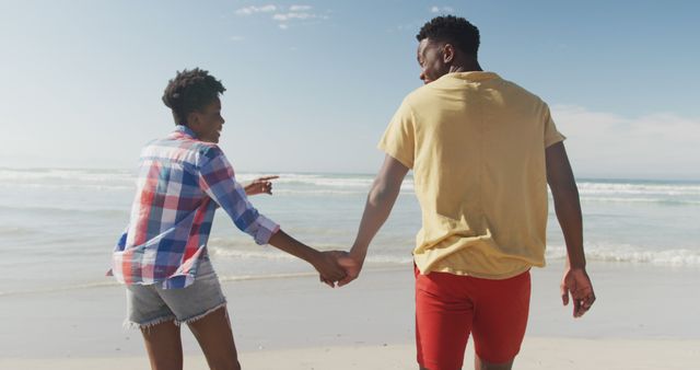 Rear view of african american couple holding hands walking on the beach. family travel and vacation concept
