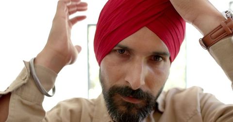 Focused man adjusting red turban at home reflecting tradition