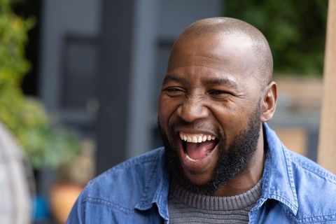 African american man laughing outdoors, candid joyful portrait in denim jacket, close-up