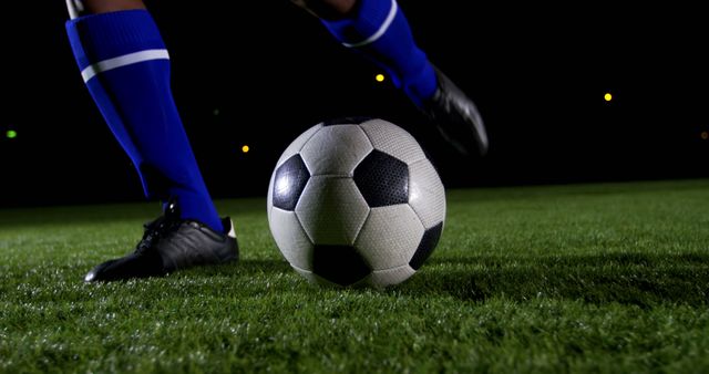 Night-time action shot of soccer player in blue socks, mid-kick, on grassy field. Great for sports articles, soccer training, youth activities, and advertisements promoting outdoor athletic gear.