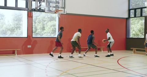 Young men playing indoor basketball passing driving shooting and defending on gym court
