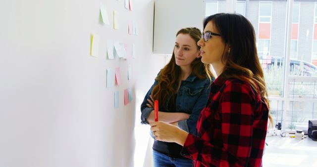 Two Businesswomen Brainstorming Ideas with Sticky Notes on Wall - Download Free Stock Images Pikwizard.com