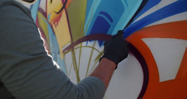 Focus shows an artist working on colorful graffiti mural. Ideal for topics on urban culture, street art techniques, creative expressions, youth culture, street artists, and public art installations.