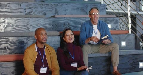 Diverse coworkers listening and taking notes at seminar on tiered benches with lanyards