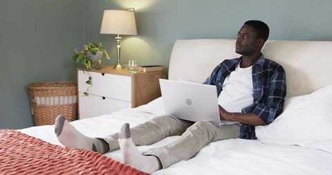 Relaxed Man Enjoying Leisure Time with Laptop in Cozy Bedroom