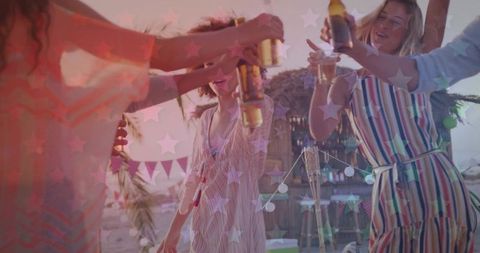 Beach party toast at dusk friends raising bottles and cups under string lights tiki bar