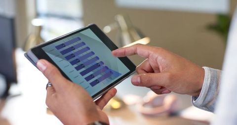 Adult male analyzing business analytics dashboard on tablet touchscreen at workspace