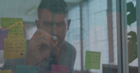 Male Professional Drawing Analytics on Glass Panel with Sticky Notes for Team Strategy