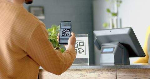 Adult female scanning qr code with smartphone at checkout counter near pos system