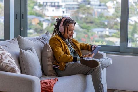 African-american man relaxing on sofa using tablet with headphones and hillside view