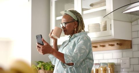 Senior Woman Relaxing with Tea and Using Smartphone in Kitchen