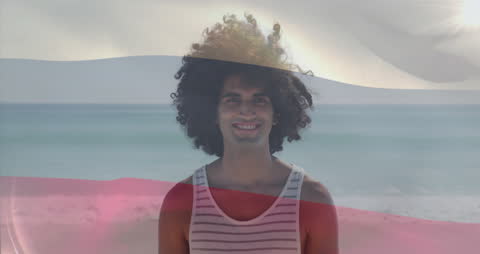 Hopeful Smiling Man on Breezy Beach Overlaid with Motion Flag