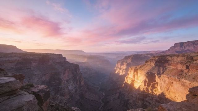 Sunrise lighting deep canyon with sunlit sandstone cliffs, misty gorge panorama