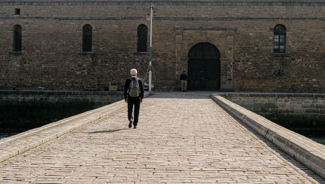 Senior man walking on historic stone bridge toward arched fortress gate