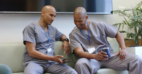 African american medical staff sharing laugh while checking smartphone during clinic break