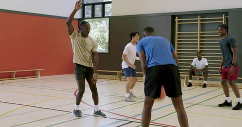 Young men playing pick-up basketball guard raising hand calling play in sunlit gym