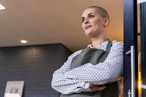 Confident retail owner standing in doorway wearing apron and polka dot blouse