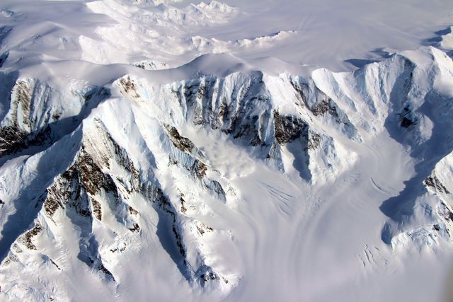This image displays an aerial view of a snow-capped mountain range in Antarctica, emphasizing the rugged and icy terrain. It can be used in articles or documentaries discussing climate change, environmental research, or polar exploration. The jagged peaks and expansive ice sheets highlight the remote and extreme conditions found in this region, making it ideal for educational materials or scientific publications focused on Earth's polar environments.