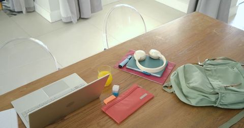 Sunlit minimalist home workspace with laptop, notebooks, headphones and pastel backpack