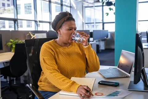 African american woman reviewing charts while sipping water at modern office desk