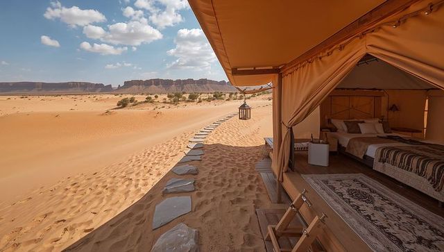 Luxury desert glamping tent on dune edge with elevated deck, stone path and mesa view