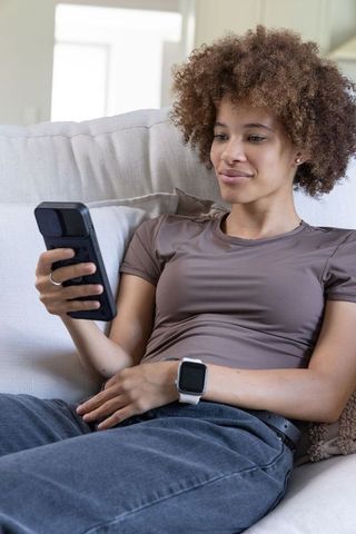 Young woman reclining on sofa using smartphone and smartwatch for relaxed tech lifestyle