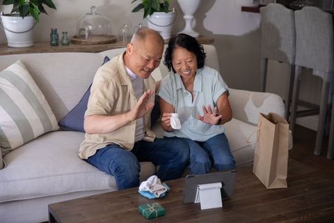 Senior chinese couple video calling family, waving and smiling on cozy living room sofa