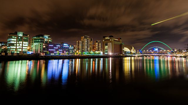 City skyline at night with brightly lit buildings reflecting on calm river water. Colorful lights creating vibrant reflections enhance urban landscape beauty. Ideal for use in travel brochures, tourism websites, posters, and urban lifestyle blogs to convey vibrant city nightlife.