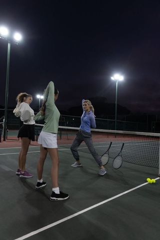 Women tennis team stretching under floodlights on night court preparing for practice session