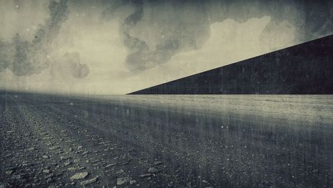 Desolate wet shoreline stretching toward distant headland under stormy monochrome sky